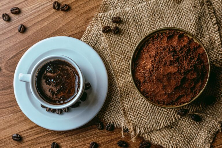 Taza de café con granos tostados y café molido sobre una mesa de madera