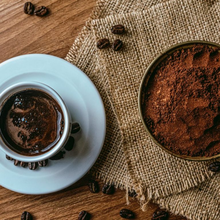 Taza de café con granos tostados y café molido sobre una mesa de madera